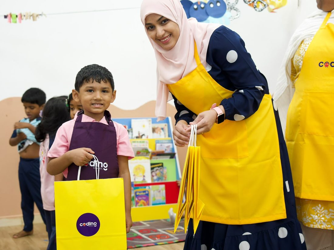 A child proudly holding a yellow Coding School take-home bag beside a facilitator.