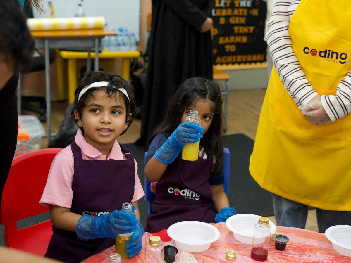 Close-up of a child in gloves mixing colourful liquids at an experiment station.