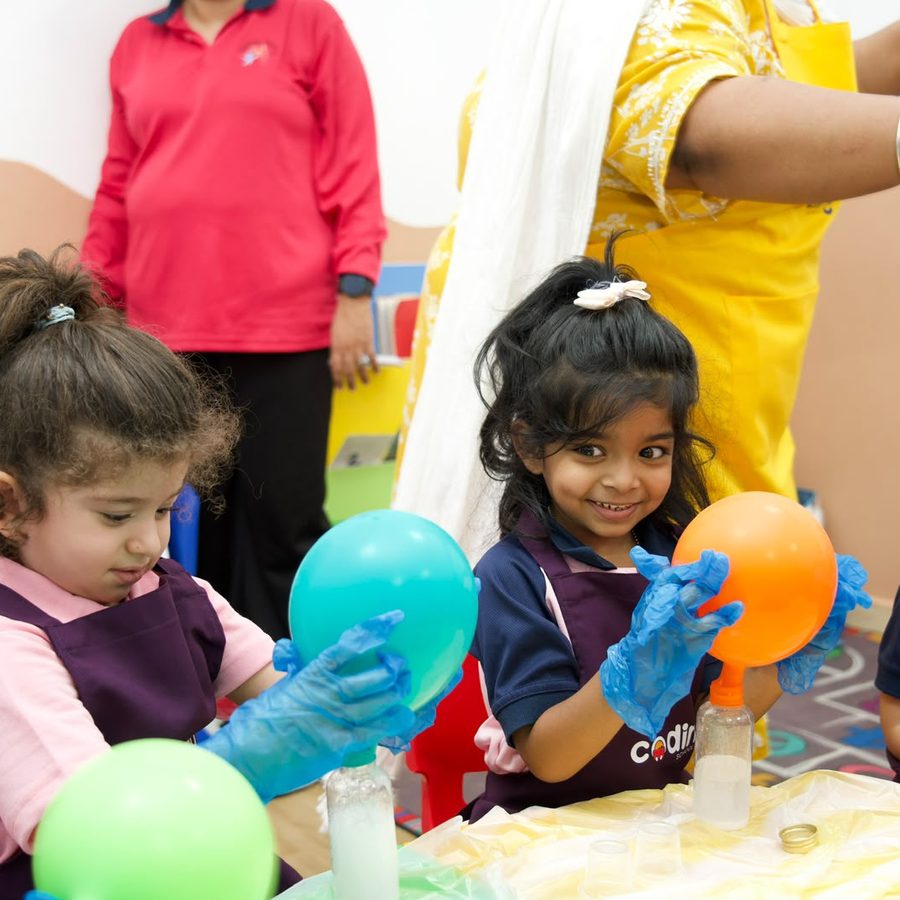 A child in blue gloves delighted by a balloon inflating over a bottle.
