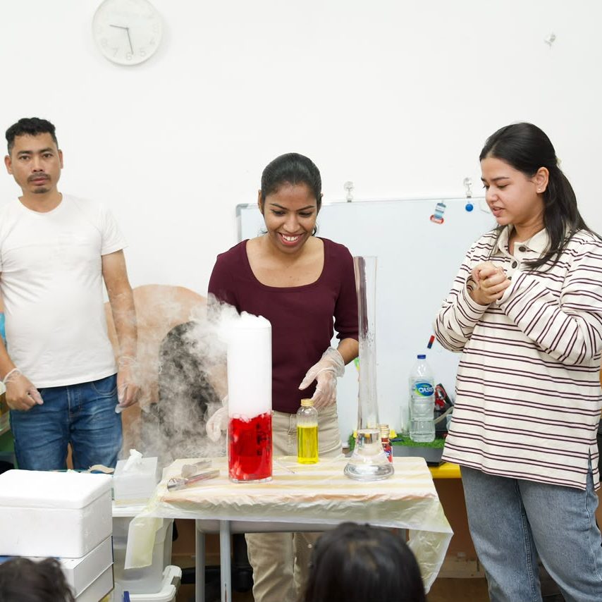 Parents and staff watching a dry ice demonstration produce billowing fog.