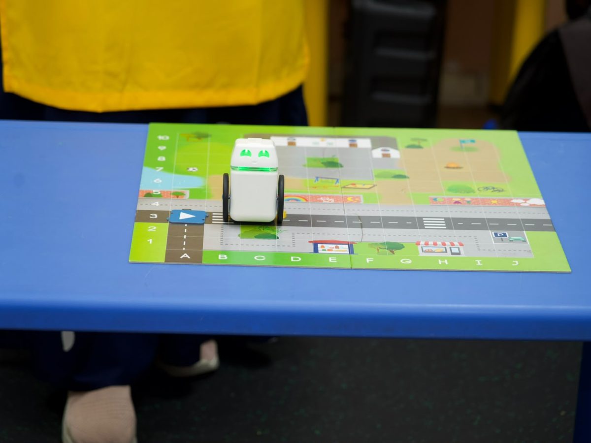 A screen-free coding robot positioned on a printed mission mat at a nursery table.