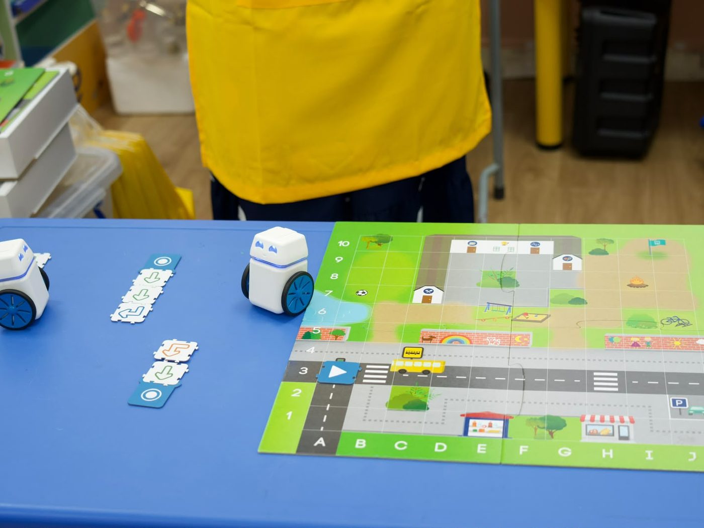 Two Kubo coding robots on a printed floor mat beside physical puzzle tiles used to program them.