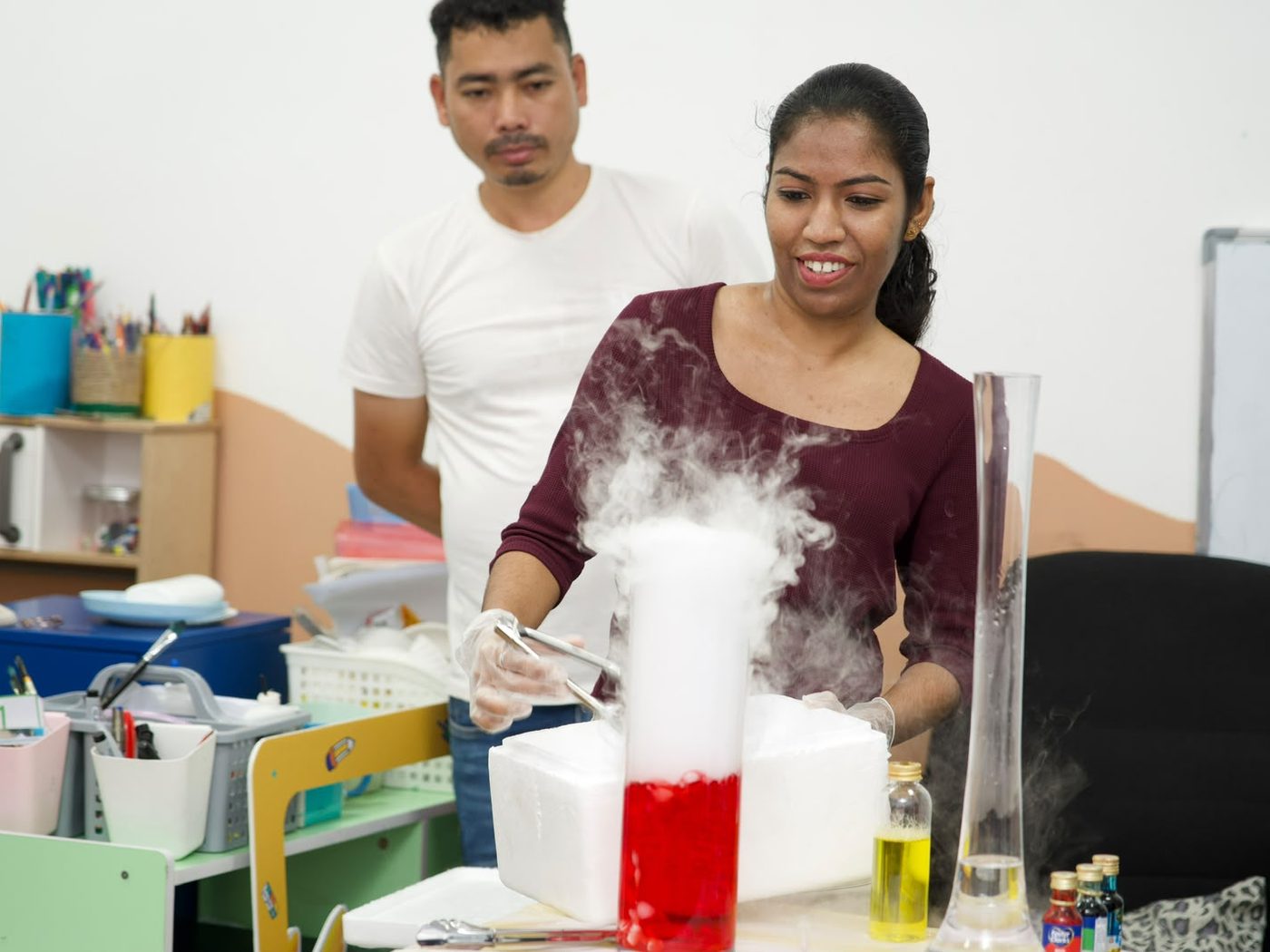 A Coding School facilitator producing a thick cloud of dry ice fog from a red container as children watch.