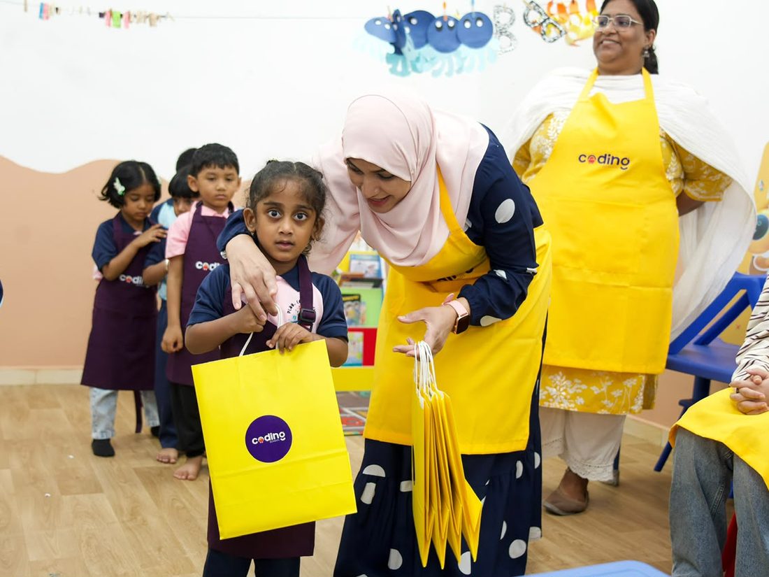 A child receiving a yellow Coding School take-home bag at the end of the day.