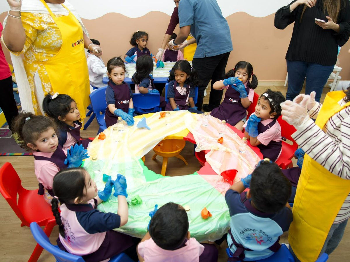 Children gathered around a large colourful collaborative creative project at a nursery table.