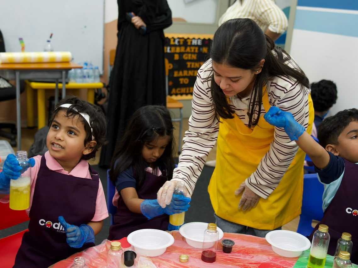 A facilitator guiding a child through a colourful mixing experiment at a nursery table.
